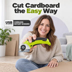 A smiling woman holding the cordless rotary scissors toward the camera, with a flat cardboard sheet beside her