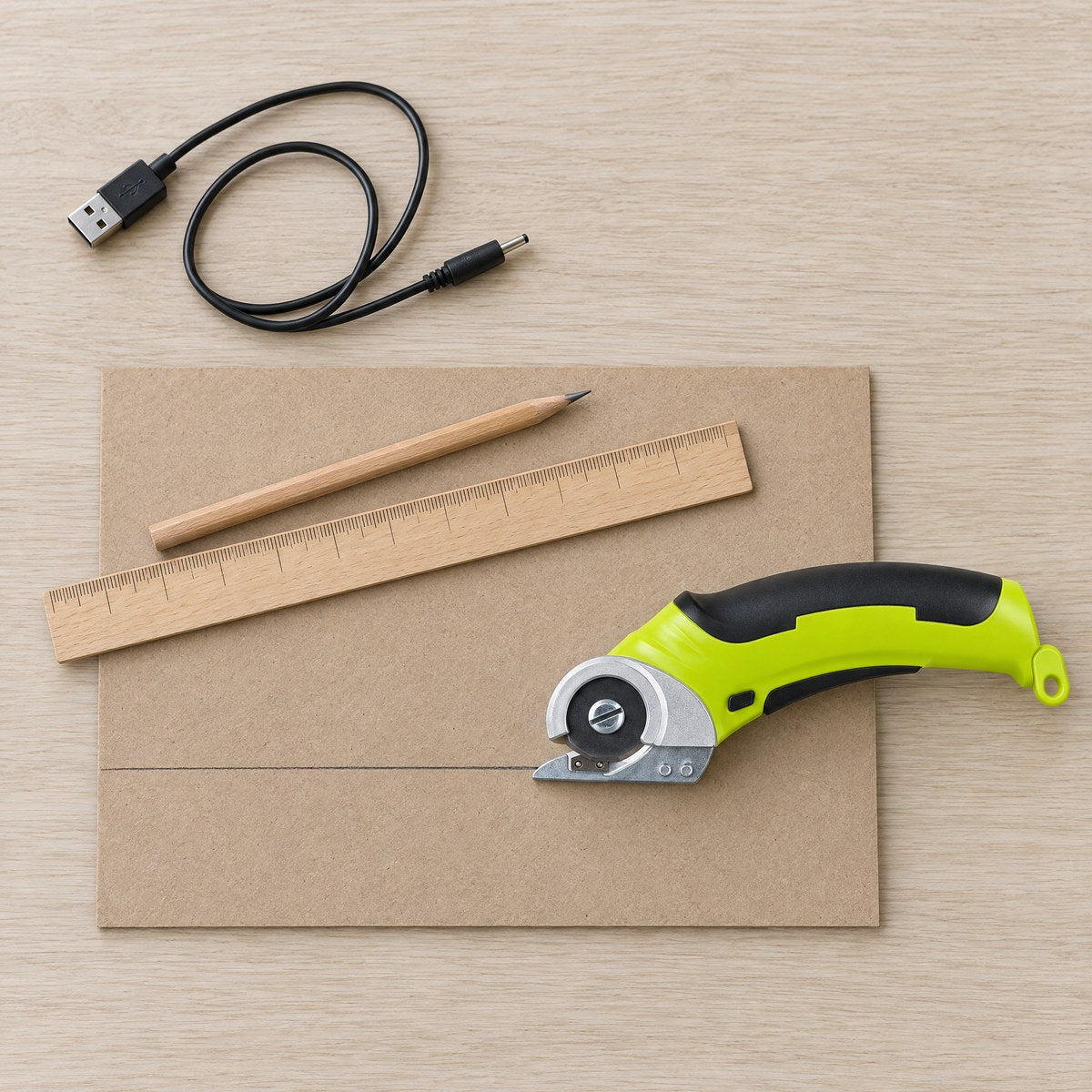 Cordless rotary scissors, USB cable, ruler and a pencil line on cardboard